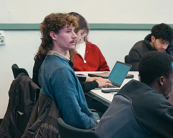 Webster Leiden students focused during a lecture, with one student taking notes on a laptop in a modern classroom.