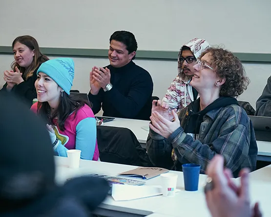 Diverse group of Webster Leiden students sitting together in a classroom, smiling and applauding during a lecture.